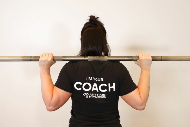 Coach holding a barbell on their shoulders, demonstrating the high-bar position.