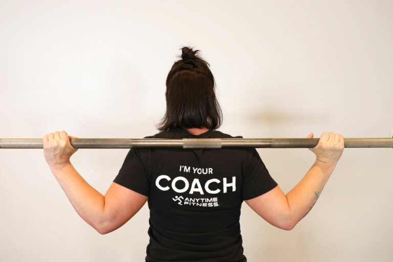 Coach holding a barbell across their shoulders, demonstrating the low-bar position.