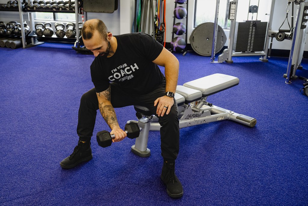 Man doing concentration curls with a dumbbell in a gym setting.