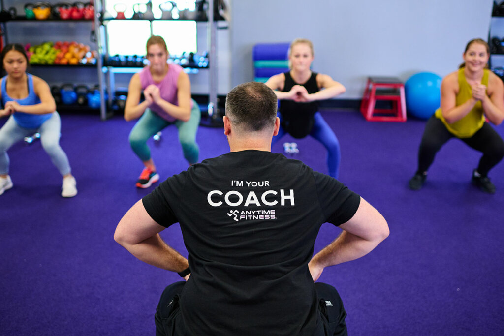 Group exercise class doing squats with Anytime Fitness Coach.