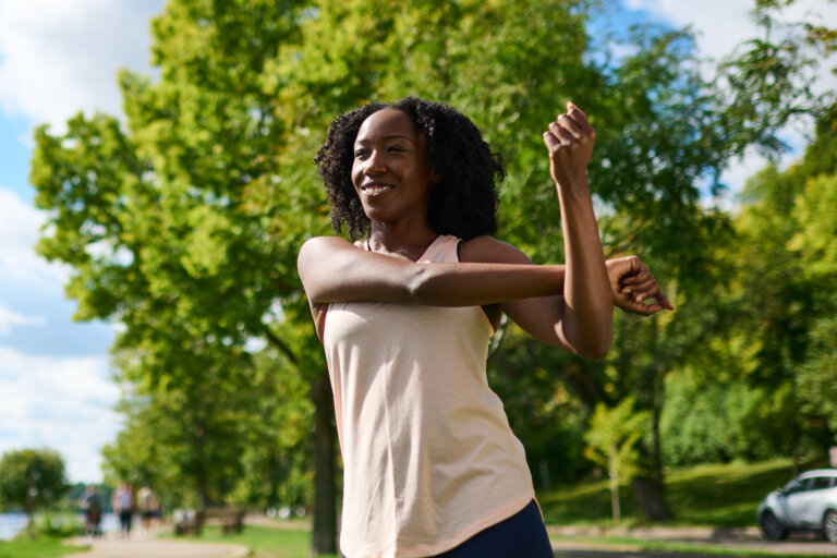 Woman outdoors performing a cross-body shoulder stretch.