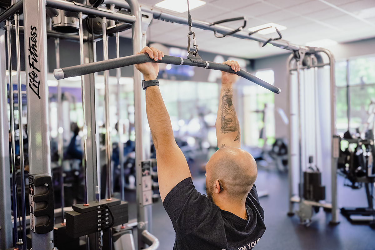 Close-up of Coach Mike demonstrating a reverse grip on the lat pulldown bar in a gym.