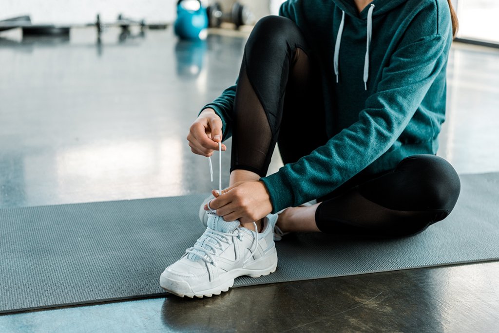 Person tying their shoe while working out in a hoodie in a gym setting.