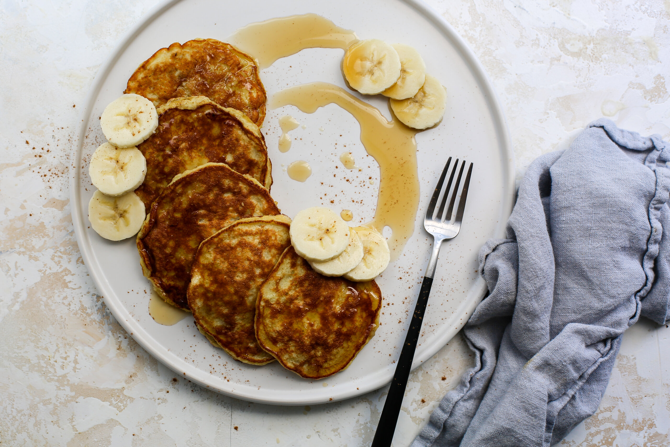 Banana pancakes on a plate with banana slices and syrup.