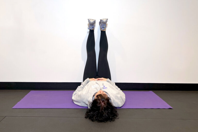 Coach lying on yoga mat with legs straight up the wall.