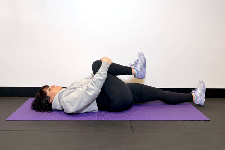 Coach lying on a yoga mat, bending right knee up toward her chest.