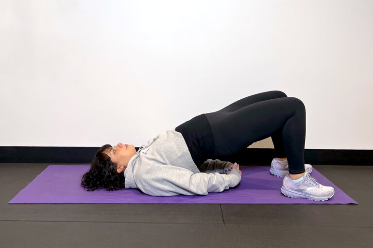 Yoga lying on a yoga mat with her hips and lower back raised in a bridge position.