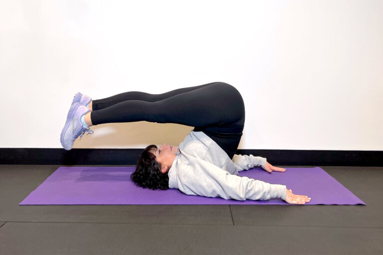 Coach lying on her back on a yoga mat with her legs stretched back over her head.