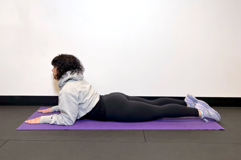 Coach lying on her stomach on a yoga mat with upper body resting on her elbows.