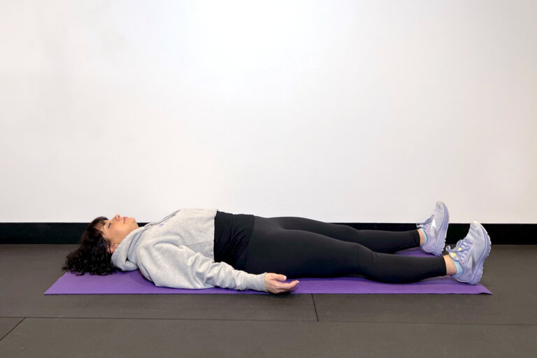 Coach lying on her back on a yoga mat with arms to her sides.