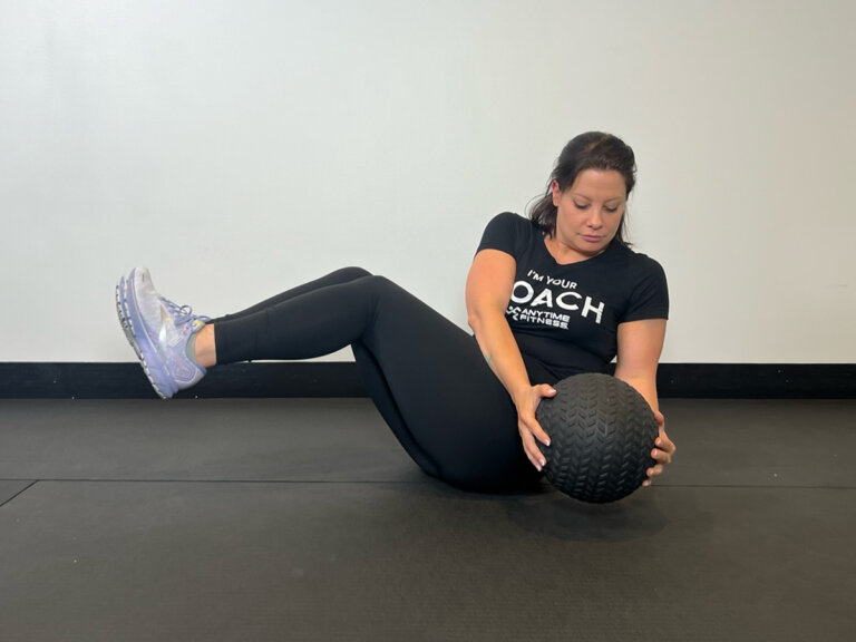 Coach seated with knees in the air, twisting medicine ball to left side.
