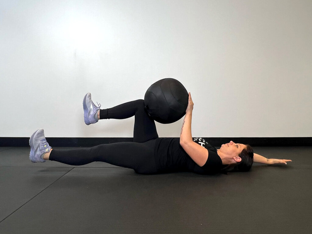 Coach raising right arm overhead and lowering left leg down to the ground.