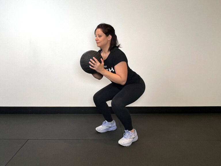 Coach in squat position holding medicine ball in front of chest.