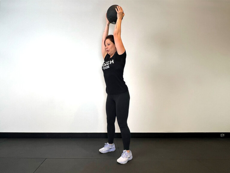 Coach standing with medicine ball raised above head.