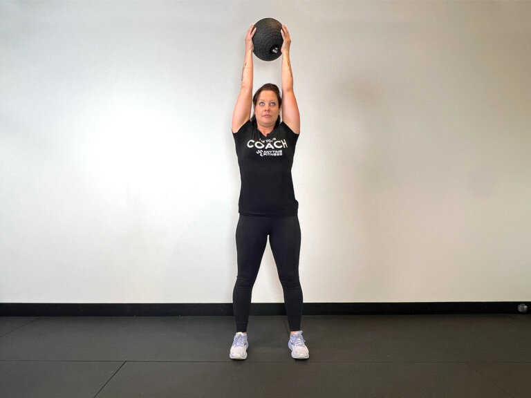 Coach standing, holding medicine ball overhead.