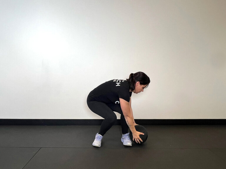 Coach in squat position, holding medicine ball outside of left foot.