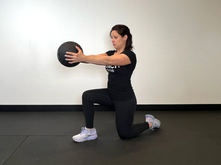 Coach in lunge position with left knee on the ground, holding ball out in front of chest.