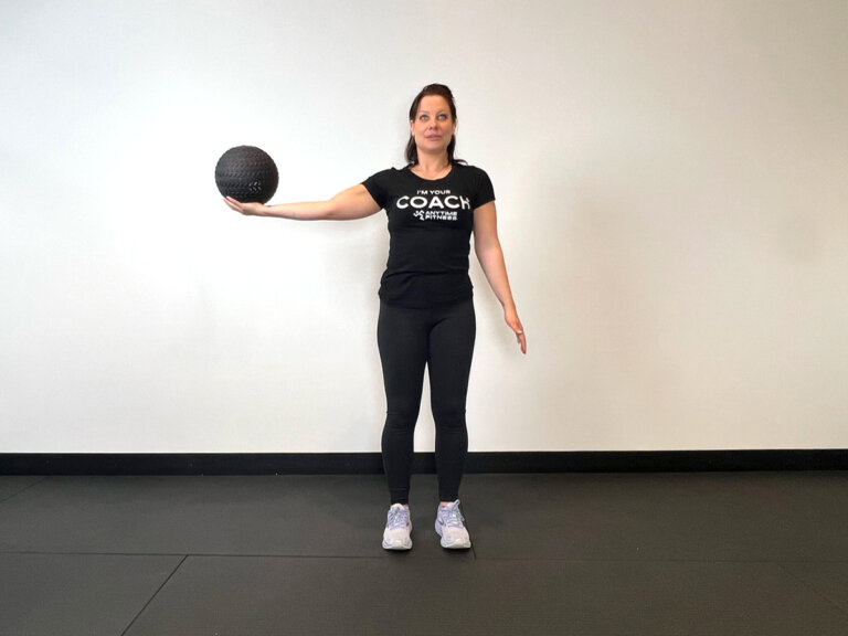 Coach standing, holding right arm out to the right with medicine ball in hand.