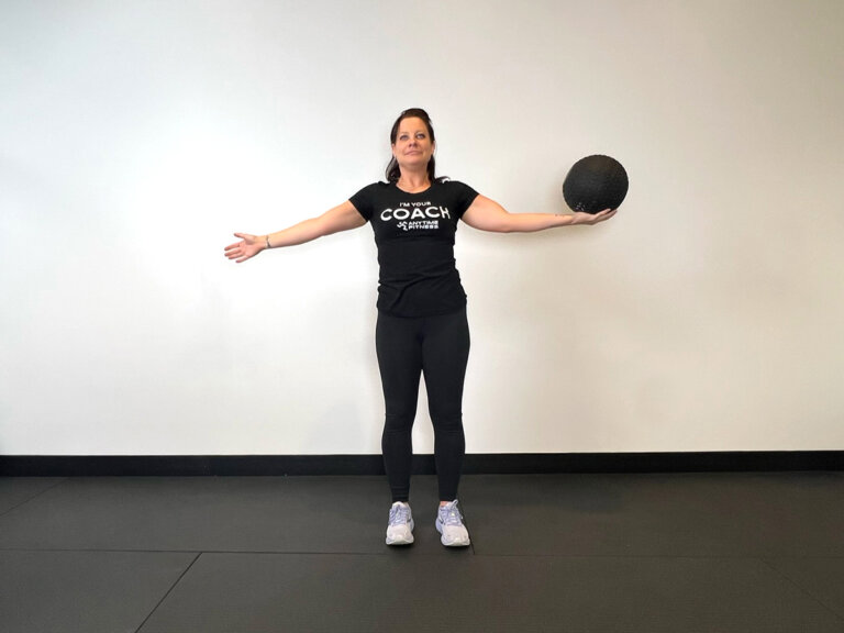 Coach standing, holding left arm out to the left with medicine ball in hand.