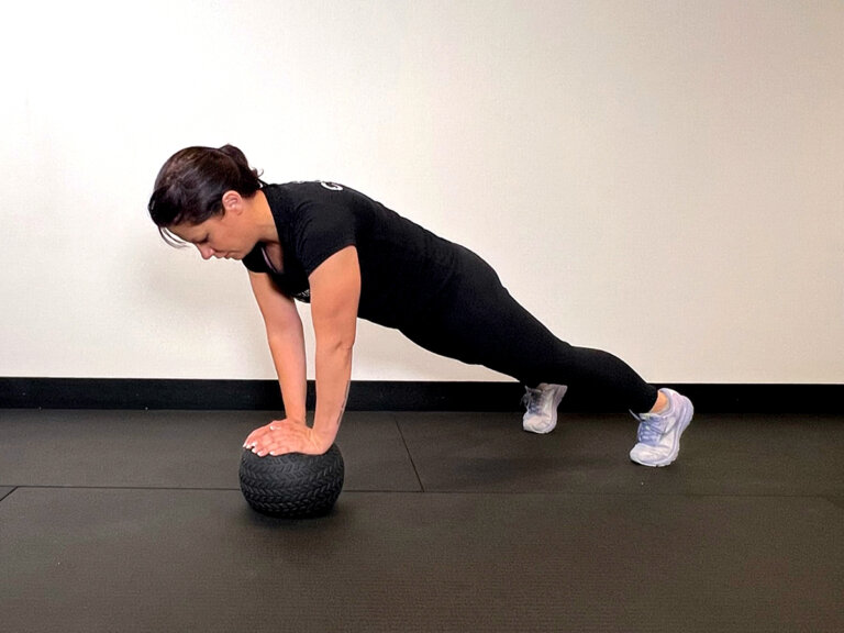 Coach does a plank while keeping both hands on a medicine ball.