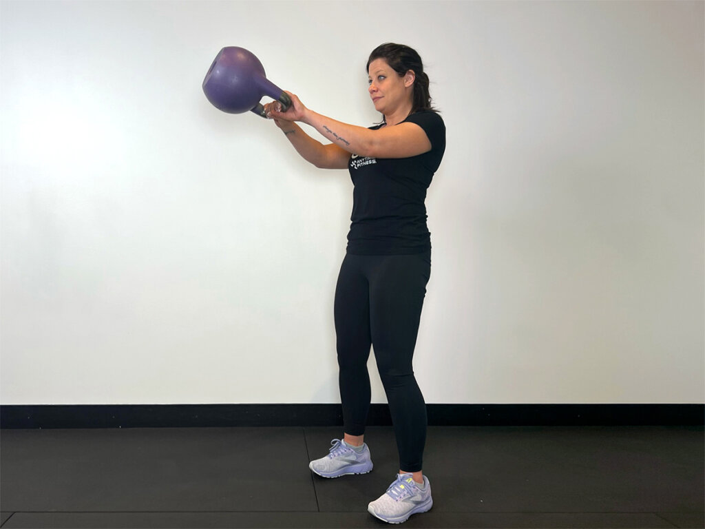 Coach swinging kettlebell up to chest-level while standing straight.