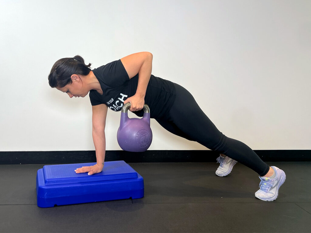 Coach pulling kettlebell to chest while remaining in plank pose.