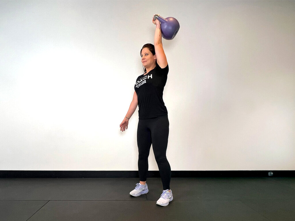 Coach lifting kettlebell overhead with a straight arm.