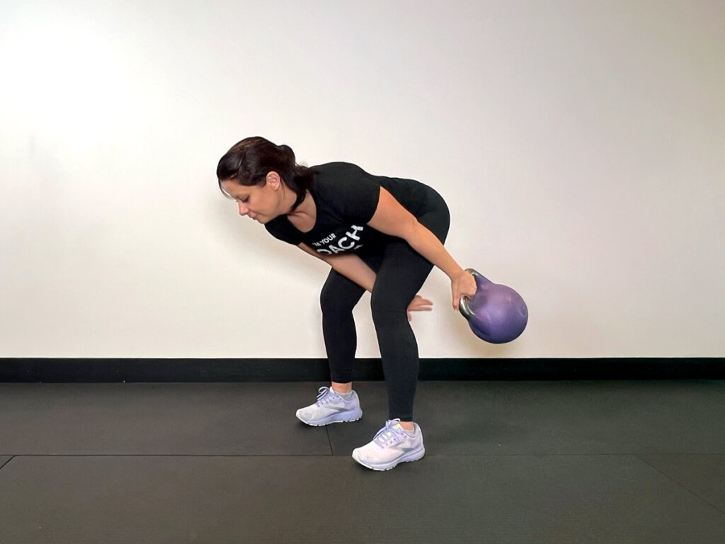 Coach using one hand to swing kettlebell around her leg, the other hand getting ready to catch the kettlebell between her legs.