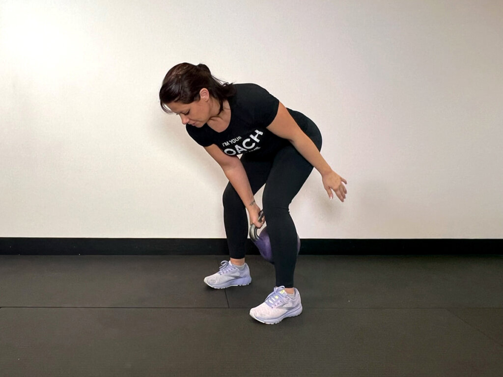 Coach catching kettlebell between legs with one hand and letting go with the other.