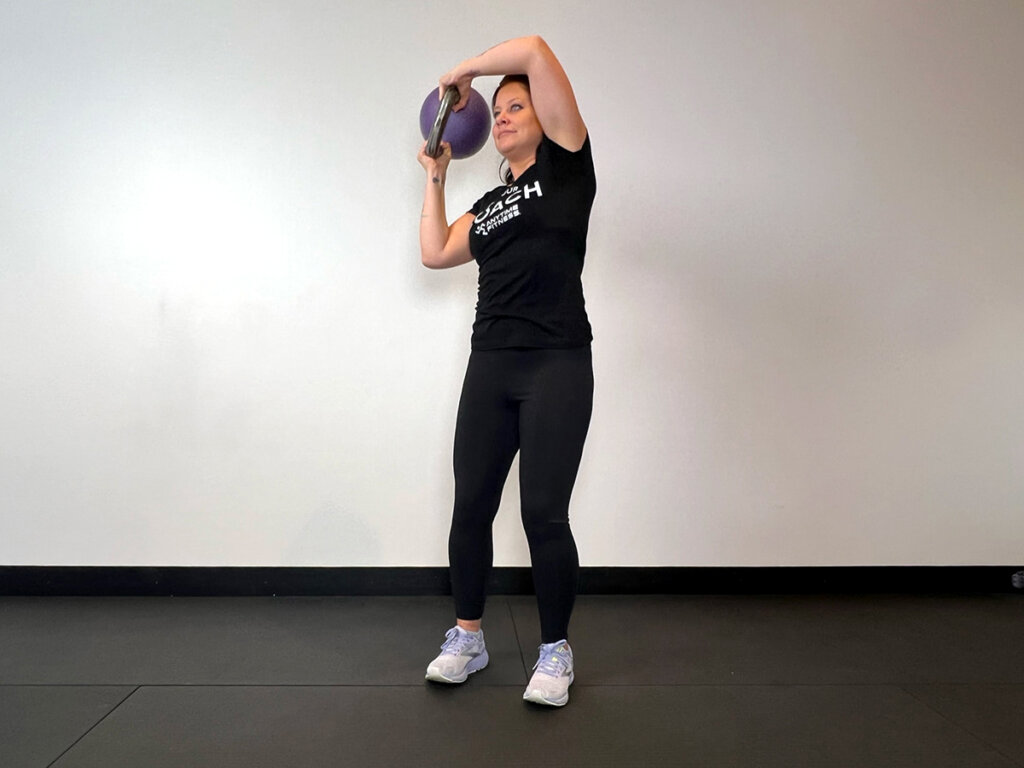 Coach continuing the halo motion, bringing kettlebell around her head.