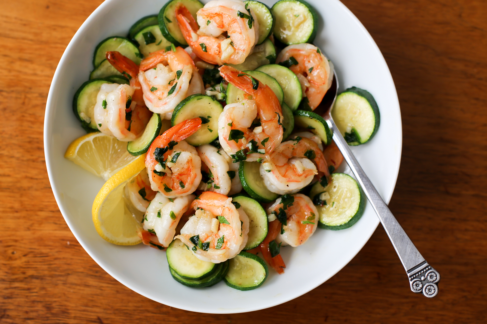 Zucchini and shrimp scampi in a white bowl with lemon slices.