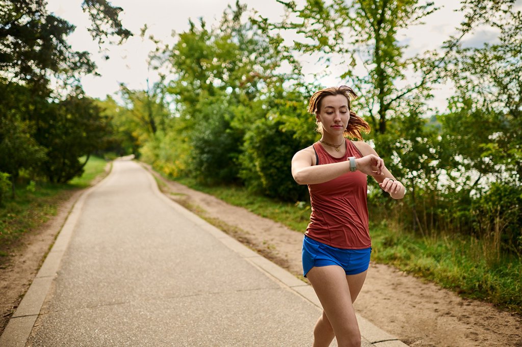 Woman running on a sidewalk, looking at her fitness watch.