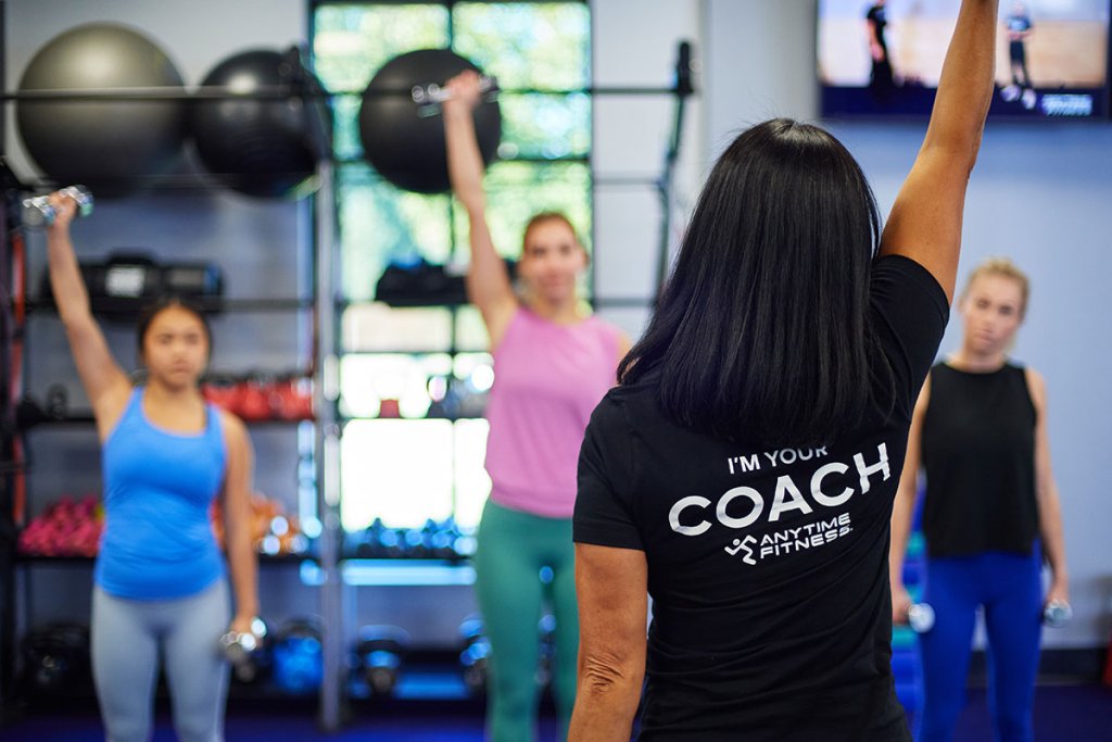 Coach leading a group exercise class in lifting a dumbbell above their heads.