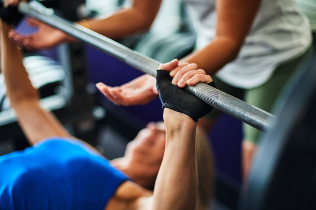 Woman doing a bench press with the assistance of her Coach.
