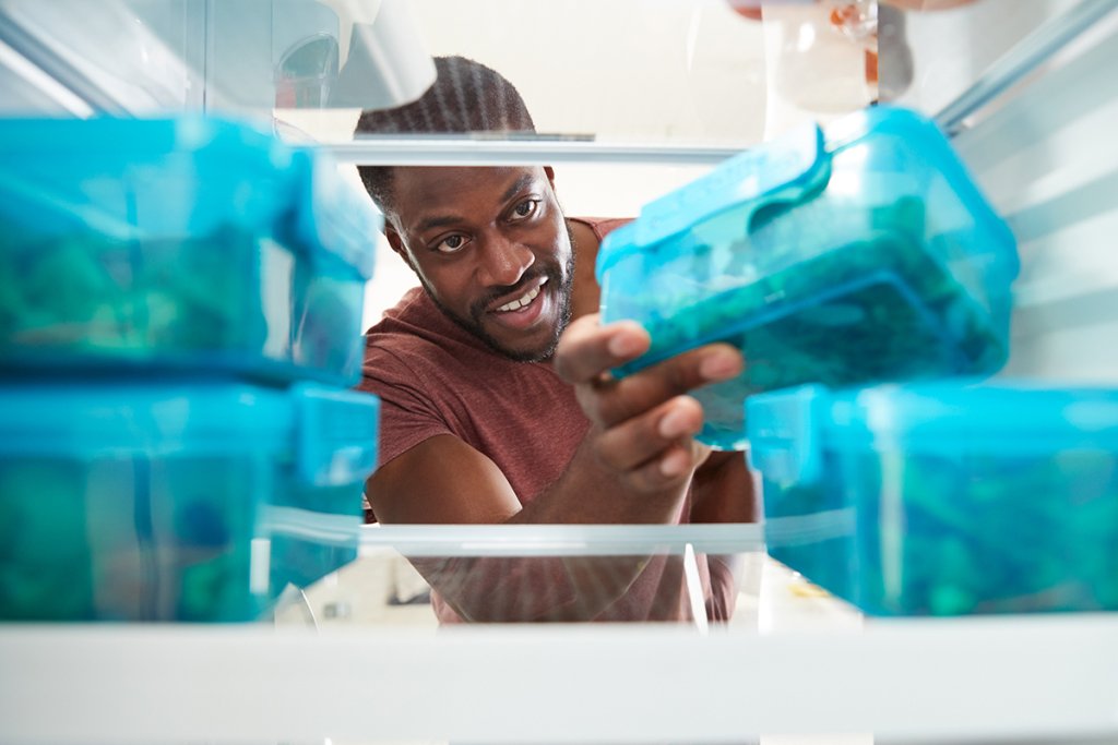Man reaching into a fridge to grab a food container.