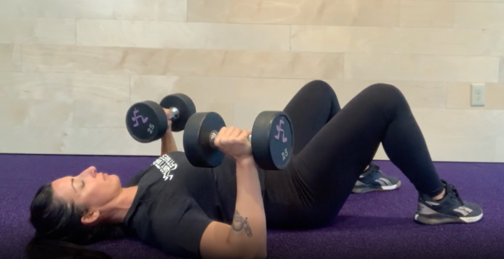 woman lying on floor performing a dumbell floor press