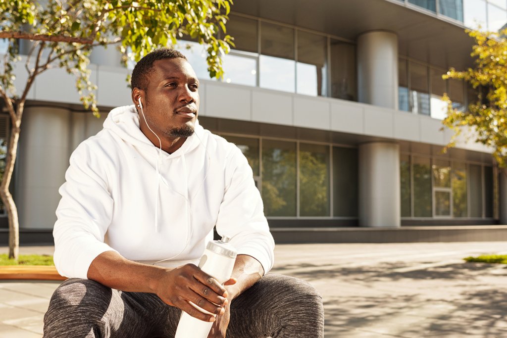 Man sitting outside a building with a white hoodie on, holding a water bottle.