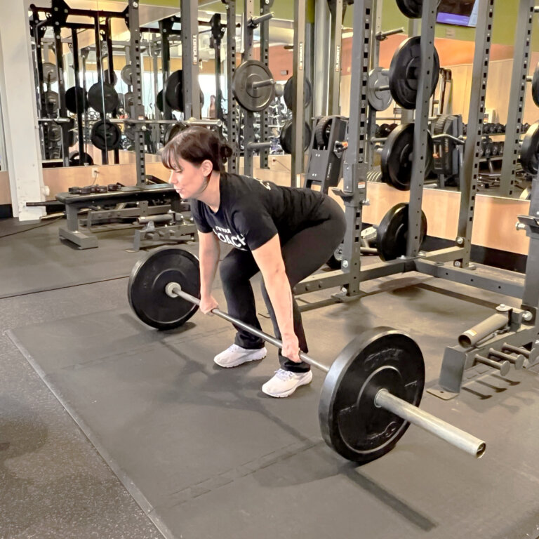Coach squatting with feet shoulder-width apart and holding the barbell with an overhand grip.