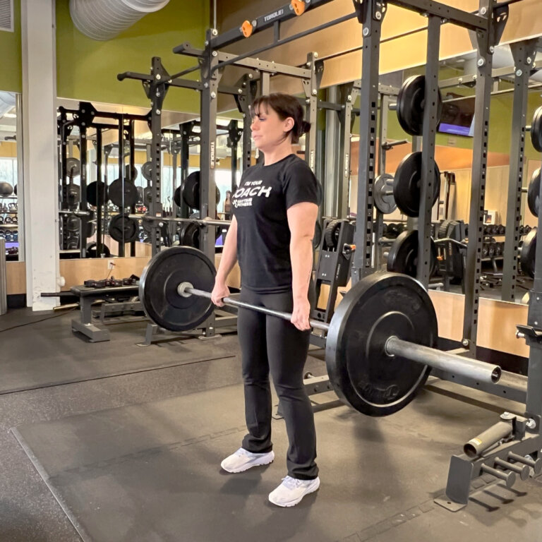 Coach standing and lifting the barbell just below the waist.