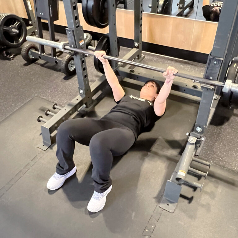 Coach hanging under the bar with arms extended and knees bent.