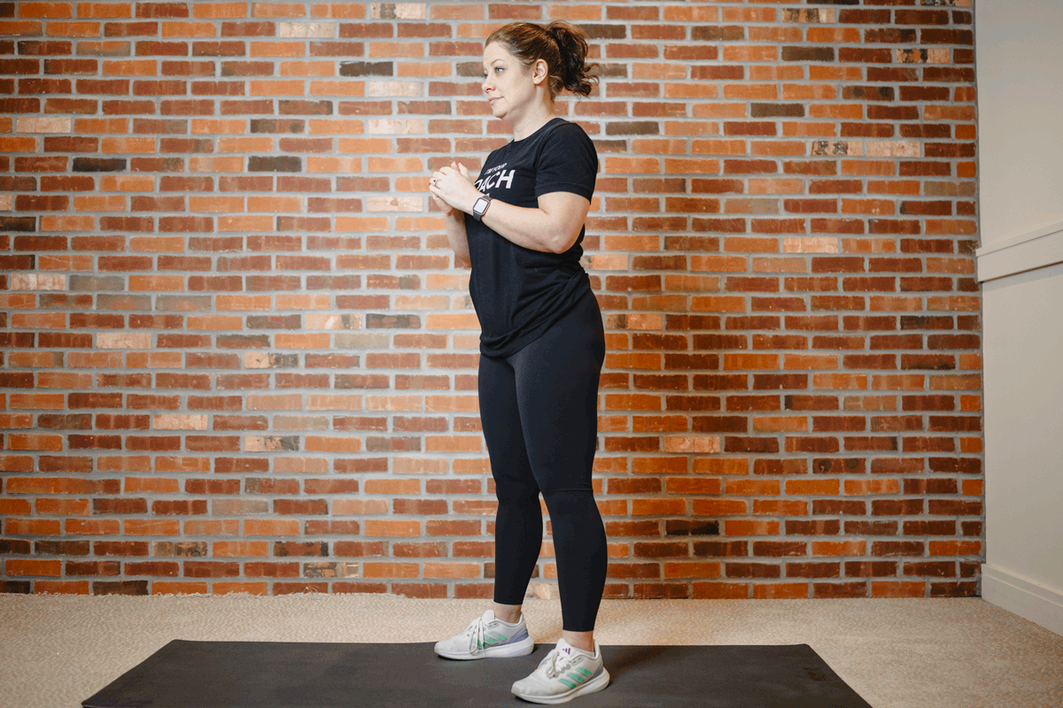 Anytime Fitness Coach performing air squats on an exercise mat in a home gym, warming up the lower body.