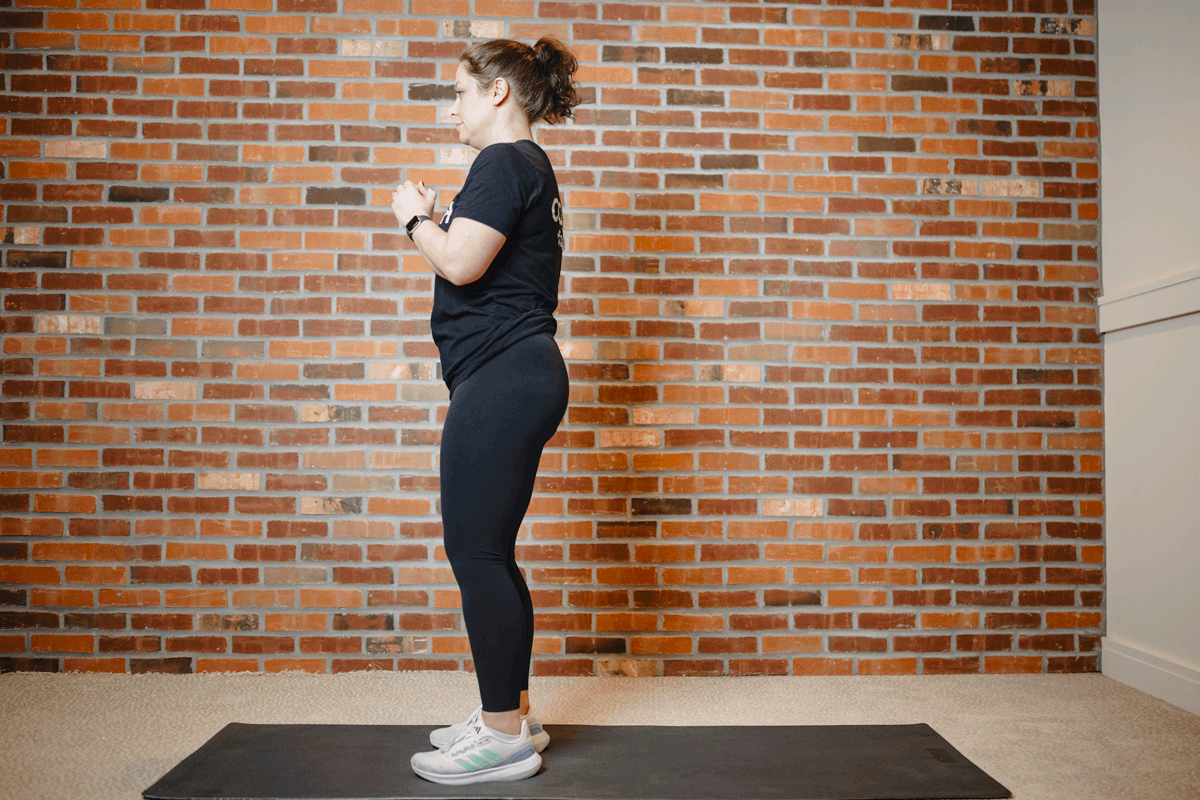 Anytime Fitness Coach performing reverse lunges on an exercise mat in a home gym, targeting lower-body muscles like the quads and glutes.