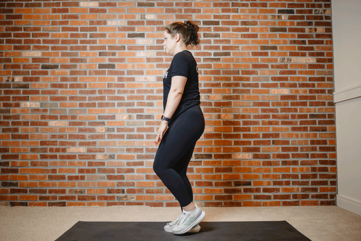 Anytime Fitness Coach performing single-leg reaches on an exercise mat in a home gym, targeting the lower body and promoting balance.