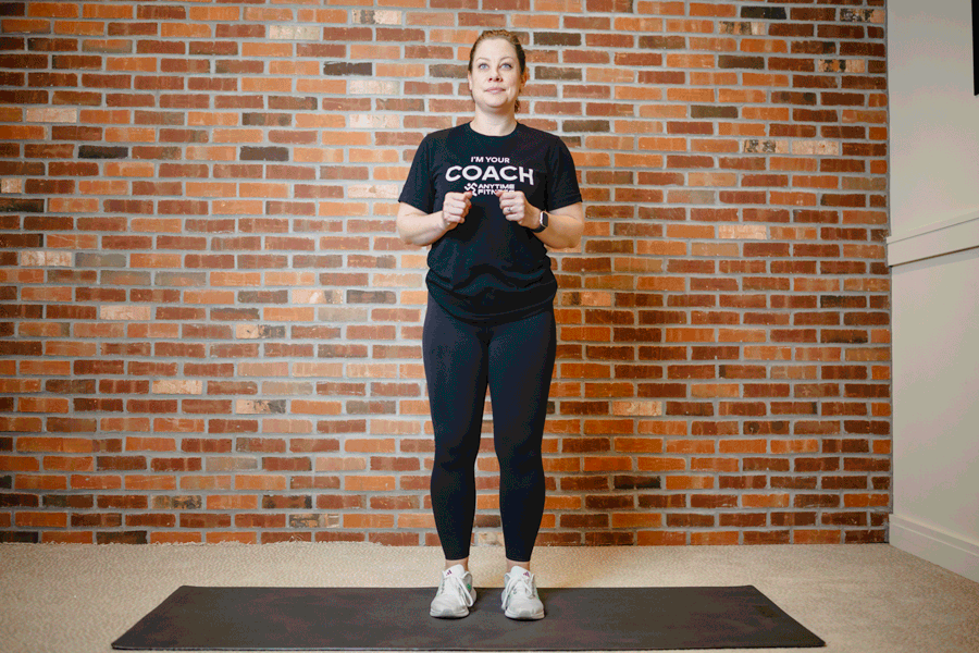 Anytime Fitness Coach performing touchdown squats on an exercise mat in a home gym for a cardio boost.