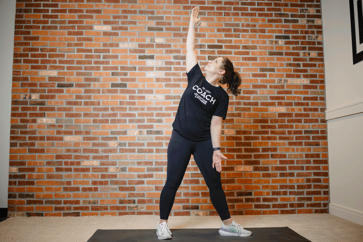 Anytime Fitness Coach performing windmills on an exercise mat in a home gym, stretching out the side body.
