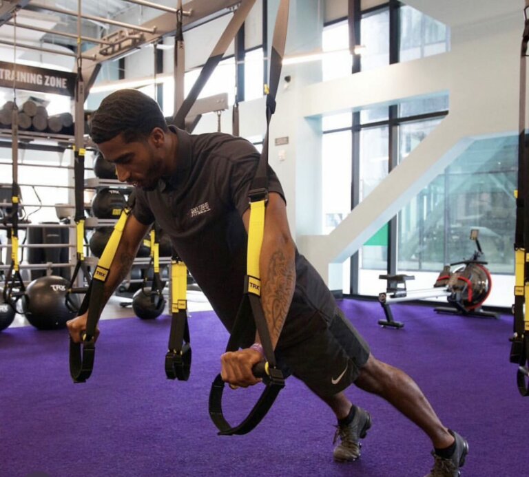 Coach exercising in a gym doing a suspended plank on stability straps.