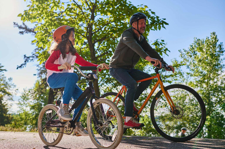 Man and child riding bicycles on a sunny path.