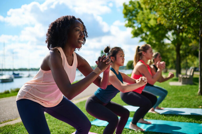 Four women doing yoga outdoors next to a lake.