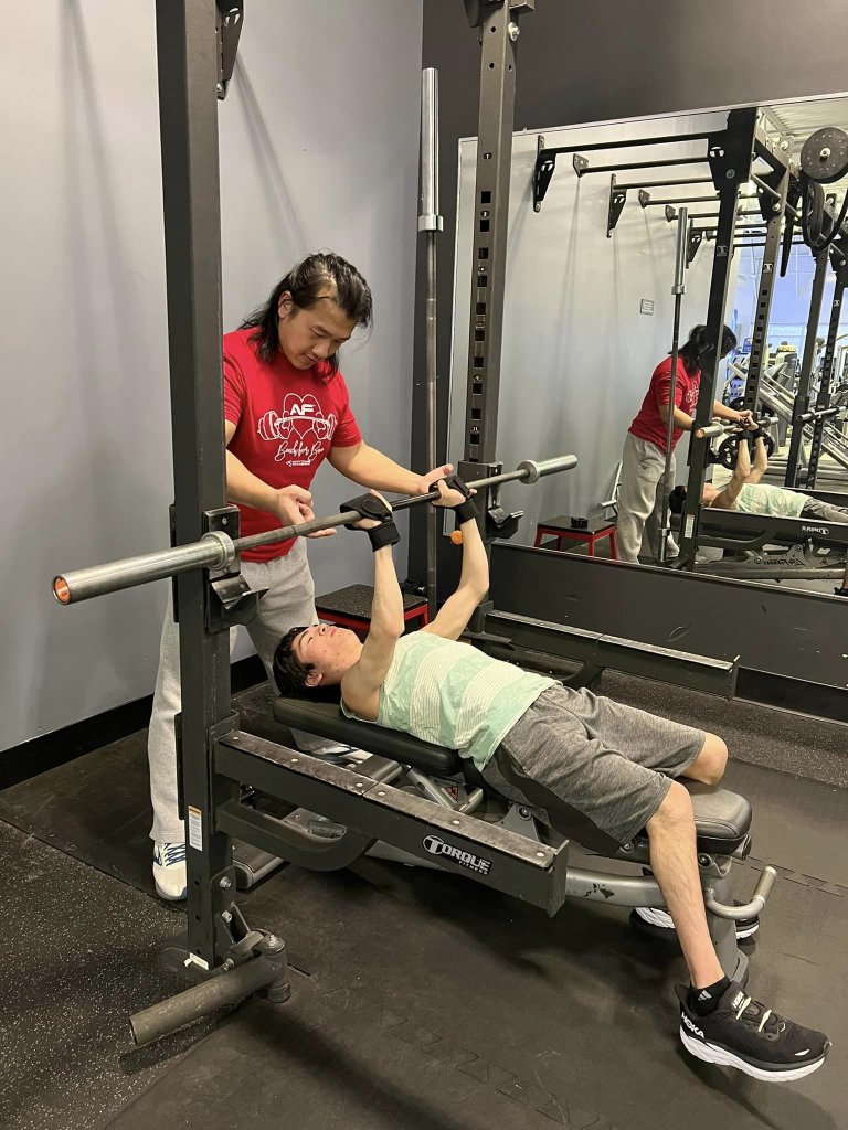 Coach Sou assisting Stephen in a bench press.