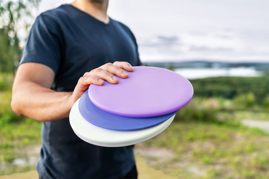 Man holding three disc golf discs in a park.